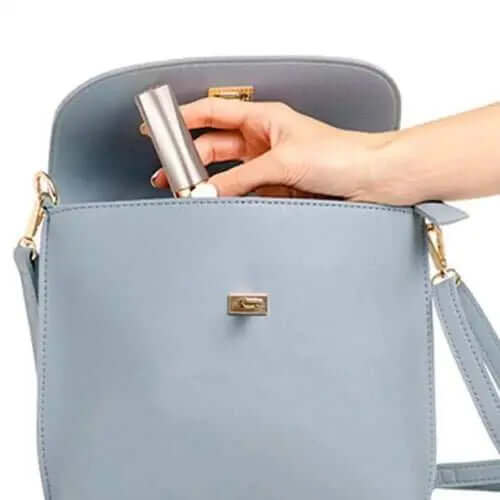 Hand placing a painless women's rechargeable shaver into a blue handbag, demonstrating portability and convenience.